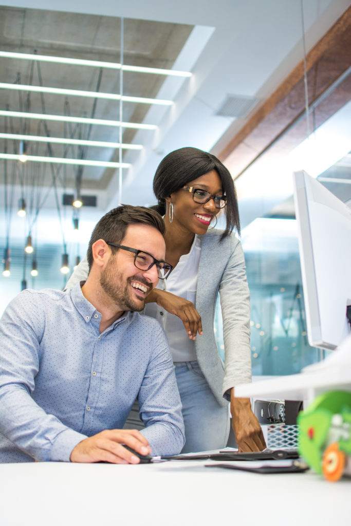 Young woman and man working together on desktop pc in the modern office