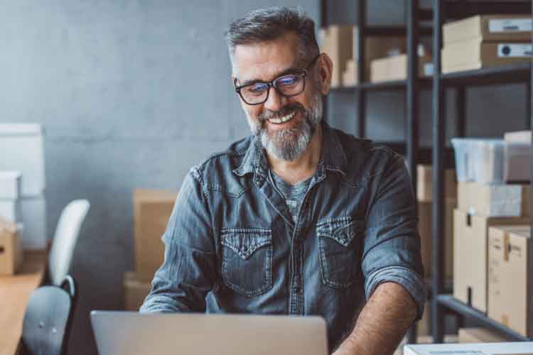 Man typing in orders to a laptop with warehouse in background